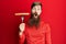 Redhead man with long beard holding fork with pork sausage scared and amazed with open mouth for surprise, disbelief face