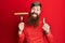 Redhead man with long beard holding fork with pork sausage smiling with an idea or question pointing finger with happy face,