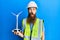 Redhead man with long beard holding solar windmill for renewable electricity scared and amazed with open mouth for surprise,
