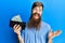 Redhead man with long beard holding wallet with polish zloty banknotes celebrating achievement with happy smile and winner