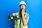 Redhead man with long beard wearing safety helmet and reflective jacket holding toolbox covering mouth with hand, shocked and