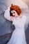 Redhead princess in a white vintage dress lying on the stones. Luxurious outfit with air sleeves. Sleeping Beauty