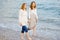 Redhead senior mother and her adult beautiful pregnant daughter are walking together on the sea shore