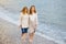 Redhead senior mother and her adult beautiful pregnant daughter are walking together on the sea shore