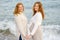 Redhead senior mother and her adult beautiful pregnant daughter are walking together on the sea shore. A happy meeting of a mom