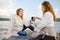 A redhead senior mother and her adult pregnant daughter are having a picnic by the sea shore. Happy meeting of a mother and her