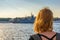 Redhead tween tourist girl on Neva river embankment looking at warships and architectural ensemble in summer evening at sunset.