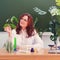 Redhead woman biology teacher in a lesson at school. Woman scientist with green plant in hand