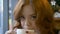 Redhead woman drinking cappuccino in cafe.