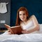 Redhead woman lying and relax on the bed and looks in her diary.