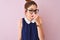 Redhead woman with pigtail wearing elegant dress and glasses over isolated pink background smelling something stinky and