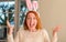 Redhead woman wearing easter rabbit ears at home very happy and excited, winner expression celebrating victory screaming with big