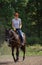 A redhead woman in white t-shirt and yellow gloves riding a horse in forest