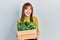Redhead young woman holding wooden plant pot smiling and laughing hard out loud because funny crazy joke