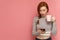 Redhead young woman holds a cup in one hand staring at her smartphone in other hand with open mouth