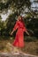 Redhead young woman in red summer country dress standing and balancing on a dry fallen tree in the middle of forest