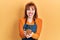 Redhead young woman wearing waitress apron holding take away cup of coffee sticking tongue out happy with funny expression