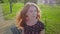 Redheaded cute young student curly hair sitting on bench outdoors in nature park with beautiful sunlight from back