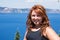 Redheaded female with long hair poses in front of the bright blue lake -Crater Lake