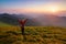 Redheaded girl athlete with a backpack and sticks stands on the green hillocks and looks at high mountain landscapes.