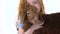 Redheaded little girl with curly hair is stroking brown lamb at white background. Slow motion. Close up