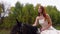 Redheaded woman in beige dress is riding horse. Close up