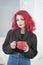 Redheaded young cheerful sad girl in knitted winter sweater holding hot tea on white room background