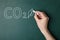 Reduce carbon emissions. Woman drawing leaf and chemical formula CO2 on green chalkboard, closeup