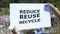 Reduce reuse recycle phrase on cardboard in hands against landfill background