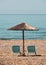 Reed beach umbrella with sunbeds on sandy beach at sea