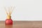 Reed diffuser with scented oil bamboo sticks in red glass bottle on wooden table white wall background. Aromatherapy home interior