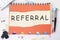 referral word is written on a sheet in a cage lying on a notebook on the table next to stationery