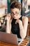 Refined business woman looking over glasses, sitting at table in