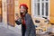 Refined curly french girl making selfie near wooden table with laptop on it. Laughing young woman in red hat taking