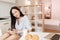 Refined young woman sits at the table with laptop and croissants on it and smiling. Gorgeous brunette lady in blue