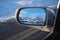 reflection of a beautiful winter landscape with mountains and village in snow in rearview mirror of car. The concept of