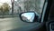 Reflection of city street and sky in auto side mirror with raindrops. Car driving in the rain. Cityscape through vehicle window.