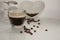 Reflection of cup of coffee and beans on reflective white background while a sugar spoon drops granules of sugar substitute into