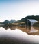 Reflection of forested mountains and old wooden building on the clear water of a lake