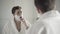 Reflection of handsome brunette man shaving with razor in bathroom. Portrait of confident Caucasian guy in white