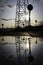 Reflection of a high voltage tower in a pond with the sky hidden behind on a cloudy evening