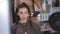 Reflection in mirror of focused woman talking as hairdresser using flat iron straightening hair. Front view of Caucasian