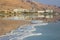Reflection of mountains, hotels and palm trees in the water of the Dead Sea with salt formations