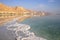 Reflection of mountains, hotels and palm trees in the water of the Dead Sea with salt formations