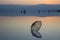 Reflection of mountains, silhouettes of people and an opened umbrella in the water of the Dead Sea at sunrise