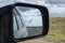 Reflections of cloudy sky, mountains and road in dirty side mirror