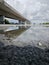 reflective pool of water on the asphalt street beneath the bridge crossing.