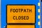 A reflective road sign with black lettering displaying FOOTPATH CLOSED