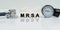 On a reflective white surface lies a stethoscope and cubes with the inscription - MRSA