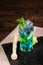 A refreshing blue lagoon cocktail with lime, mint, ice, bilberries and decorative carambola on a wooden background. Copy space.